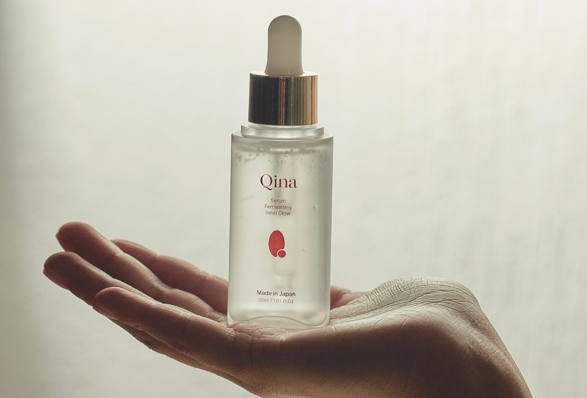 Sérum Qina sostenido sobre una mano abierta con fondo luminoso